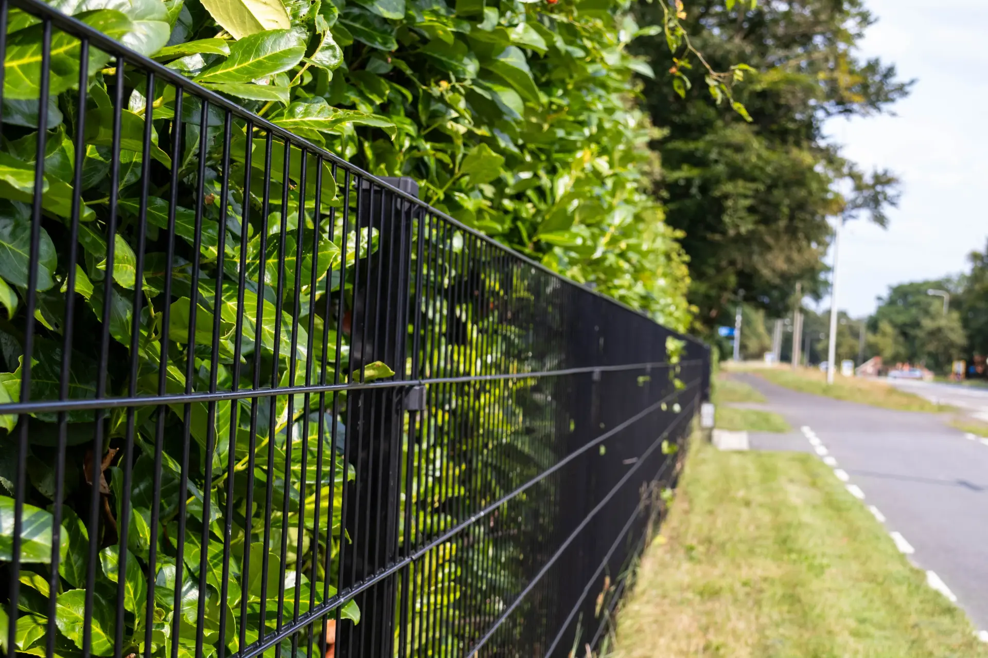 Zwart dubbelstaafmat bedrijfshekwerk langs een weg